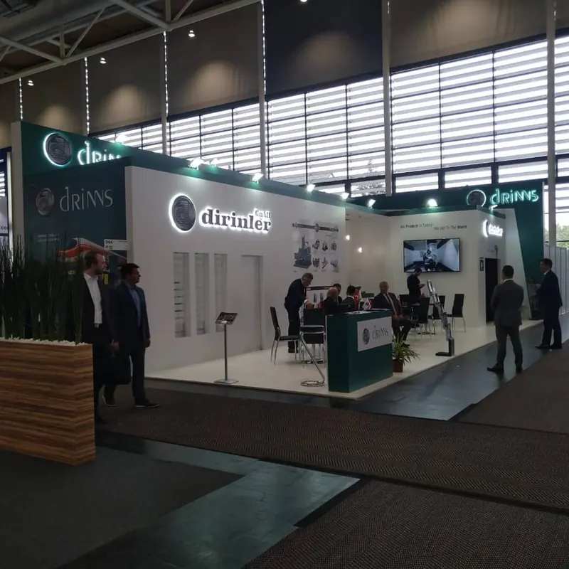 Weiß-grüner offener Messestand mit großen Markenwänden und Besuchern.