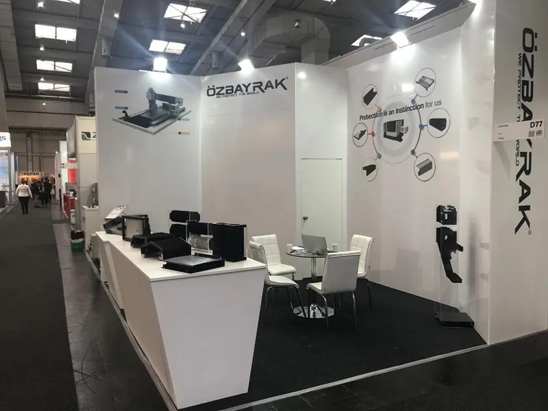 Weißer Messestand mit schwarzen Bauteilmustern auf langer Theke und weißen Stühlen.