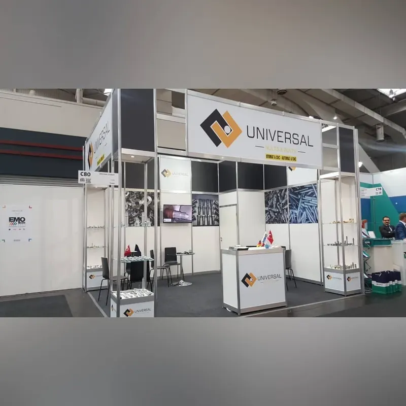 Weißer Messestand mit hohen Rahmen, schmalen Produktpodesten und schwarzen Stühlen.