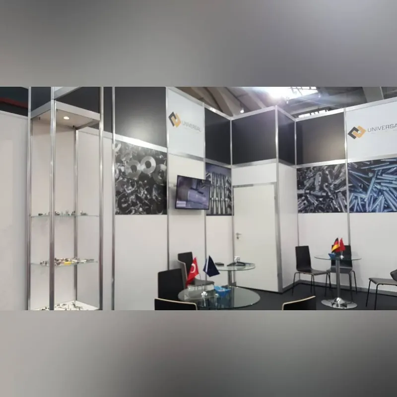 Weiß-schwarzer Messestand mit Glasvitrine, Metallteilgrafiken und schwarzen Sitzgruppen.
