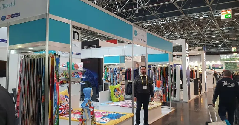 Türkis-weißer Messestand mit langen Stoffbahnen und Besuchern im Messegang.