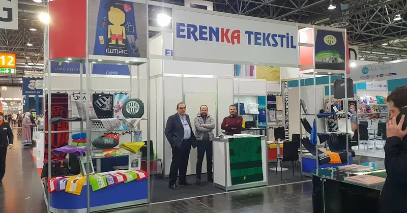 Weiß-blauer Messestand mit bunten Stoffmustern und Personen vor einer kleinen Theke.