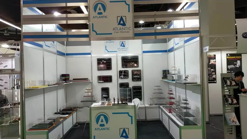 Weiß-blauer Messestand mit Glasvitrinen, offenen Regalen und hohen Rahmen.