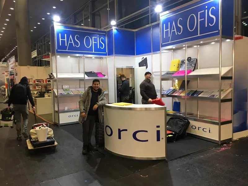 Blau-weißer Messestand mit offenen Regalen, Produktmustern und gerundeter Theke.