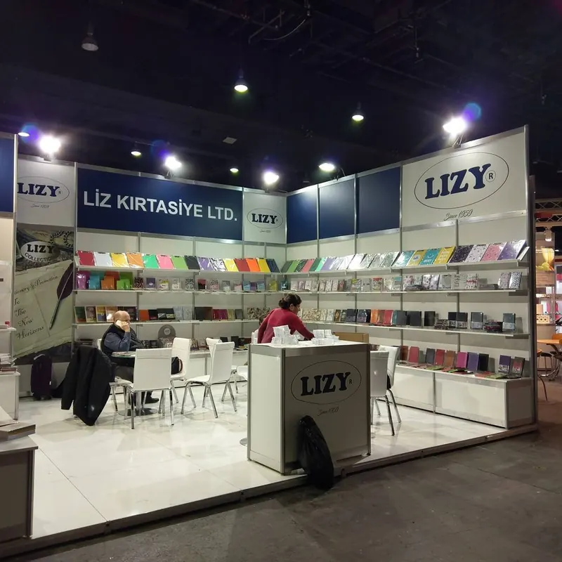 Weiß-blauer Messestand mit Regalen voller bunter Produkte und Personen an der Sitzgruppe.