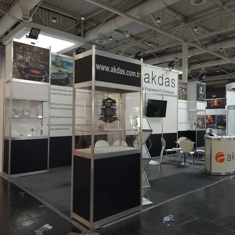 Weiß-schwarzer Messestand mit Glasvitrinen, Bildschirm und ausgestellten Metallteilen.