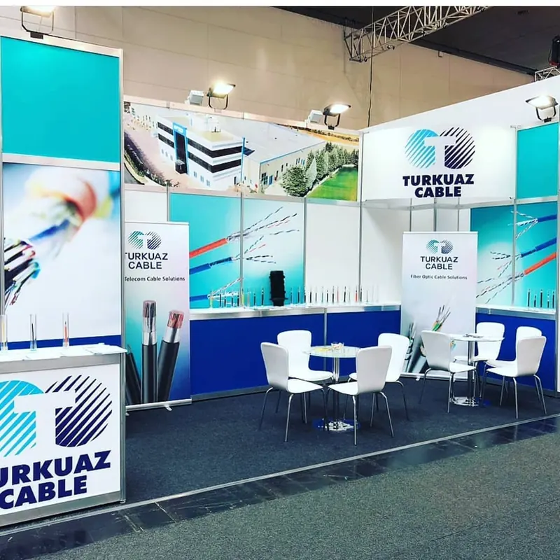 Türkis-weißer Messestand mit Kabelmustern, blauen Wandflächen und weißer Sitzgruppe.