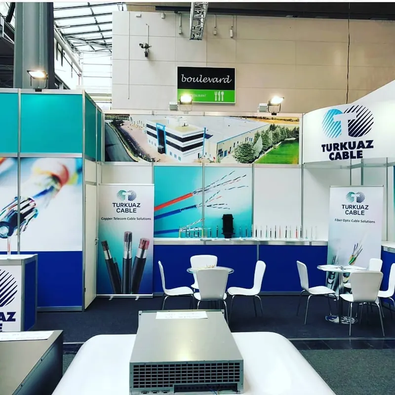 Weiß-blauer Messestand mit türkisfarbenen Kabelgrafiken und weißen Sitzgruppen.