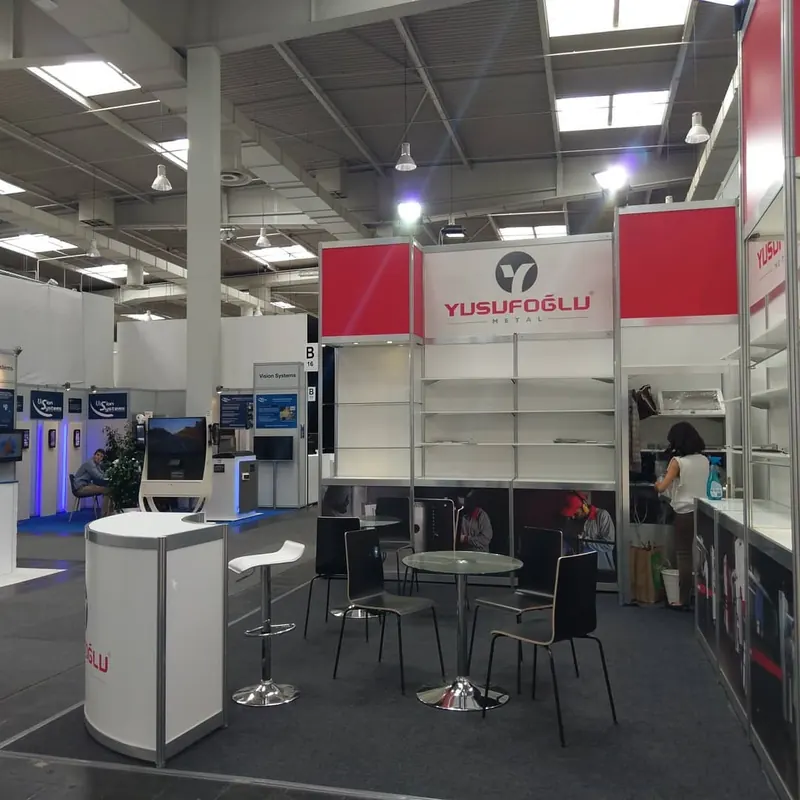 Weiß-roter Messestand mit Glasregalen, runden Tischen und schwarzen Stühlen.