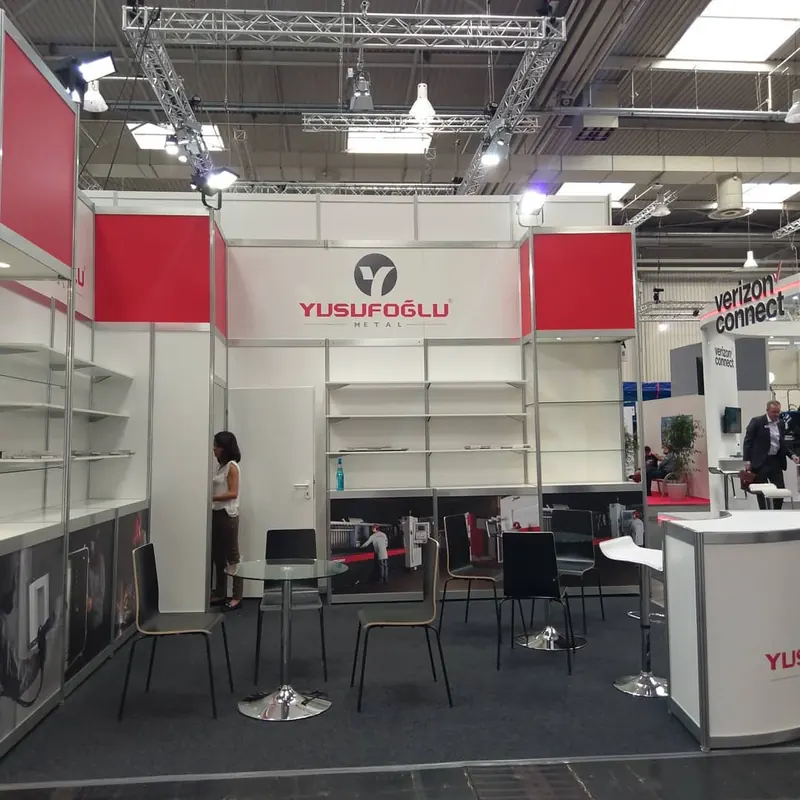 Weiß-roter Messestand mit offenen Wandregalen und einer weißen Empfangstheke.