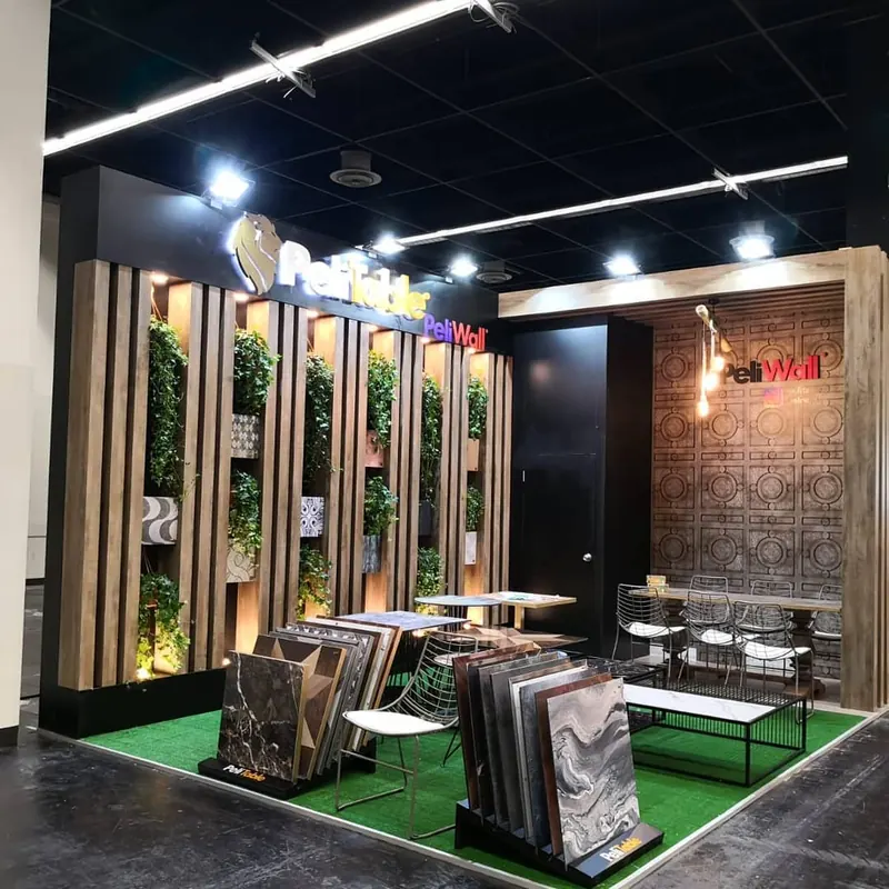 Dunkler Messestand mit Holzoptiklamellen, Pflanzen, Materialmustern und grünem Boden.