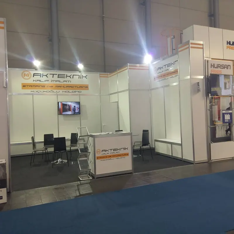 Weißer Messestand mit Bildschirm, Prospektständer und schwarzer Sitzgruppe.