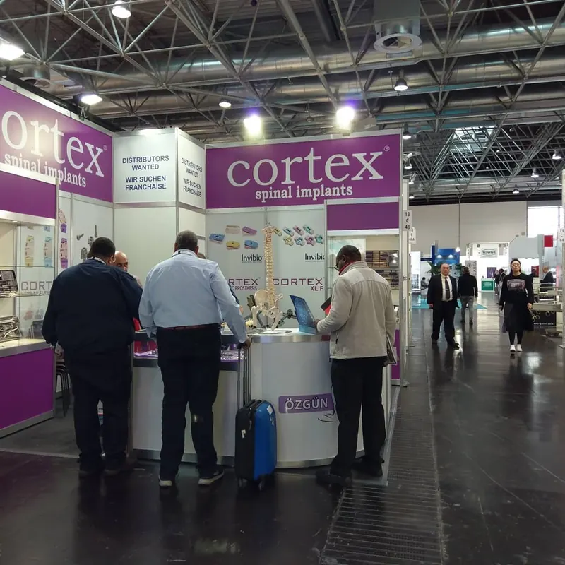 Weiß-violetter Messestand mit Produktvitrinen und Besuchern an einer kleinen Theke.