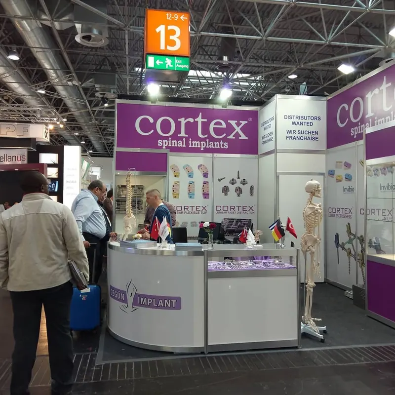 Weiß-lila Messestand mit geschwungener Empfangstheke, Skelettmodell und Personen am Stand.