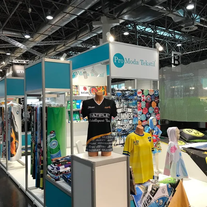 Türkis-weißer Messestand mit bunten Bekleidungsmustern und hellen Produktpodesten.