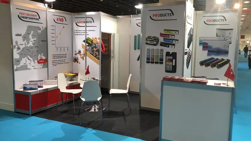 Weiß-roter Messestand mit farbigen Produktbildern, heller Theke und weißen Stühlen.