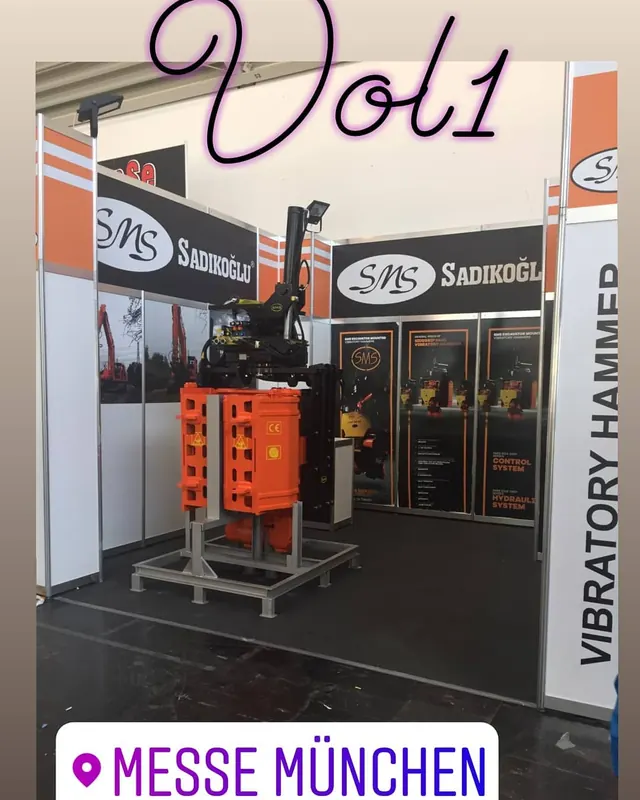 Weiß-oranger Messestand mit einer großen orangefarbenen Maschine auf einem Metallgestell.