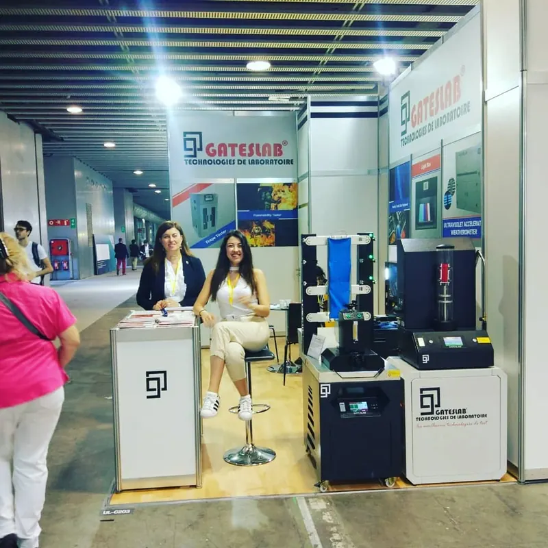 Heller Messestand mit Produktpodesten, schwarzen Geräteexponaten und Personen an einer Theke.