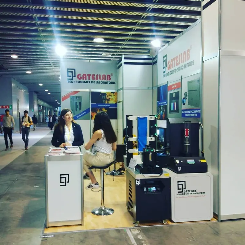 Weiß-blauer Messestand mit technischen Exponaten auf Podesten und Personen an der Theke.