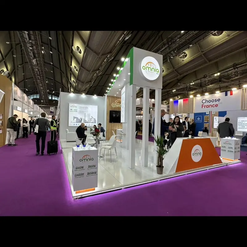 Weißer offener Messestand mit orangefarbenen Theken und violettem Hallenteppich.