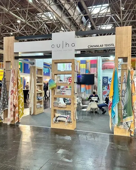 Messestand mit Holzoptikrahmen, farbigen Stoffmustern und einem zentralen Spiegel.