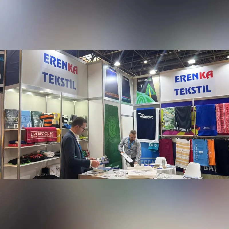 Weißer Messestand mit farbigen Stoffmustern und Menschen an einem Tisch.