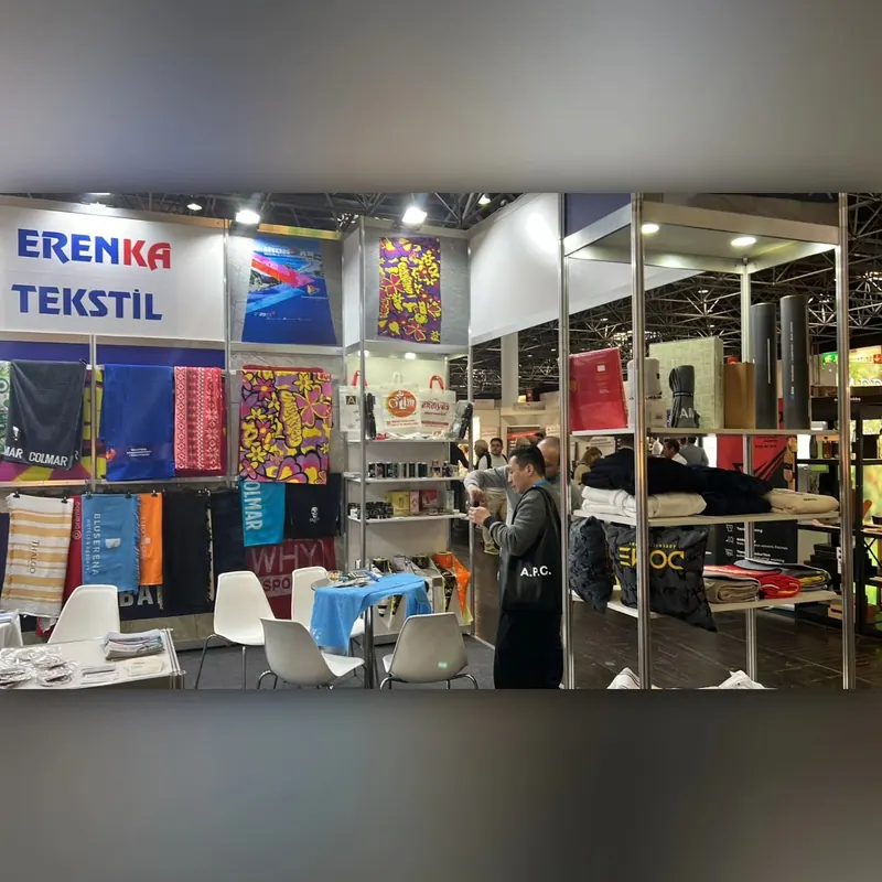 Weißer Textilstand mit farbigen Stoffen in Regalen, Sitzgruppe und Personen am Stand.
