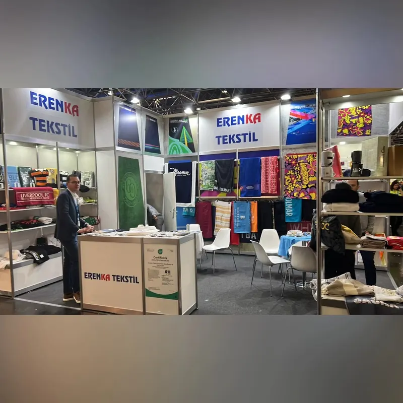 Weißer Textilstand mit farbigen Stoffen in Regalen, Sitzgruppe und Personen am Stand.
