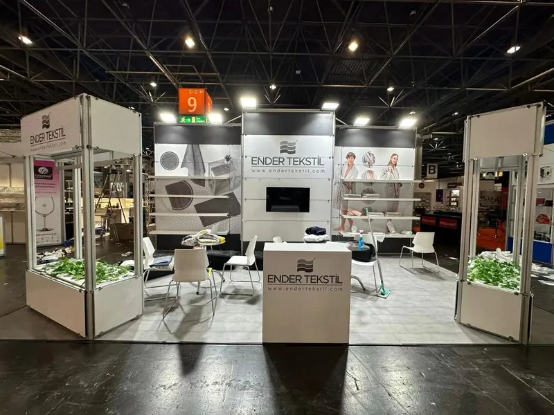 Weißer offener Messestand mit großen Fotowänden, heller Sitzgruppe und Pflanztrögen.