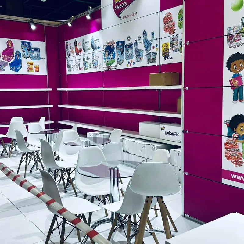 Pink-weißer Messestand mit bunten Verpackungsmotiven, Regalen und weißen Sitzgruppen.