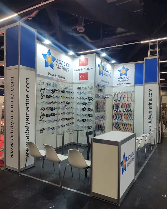 Blau-weißer Messestand mit Werkzeugmustern an den Wänden und weißen Stühlen.