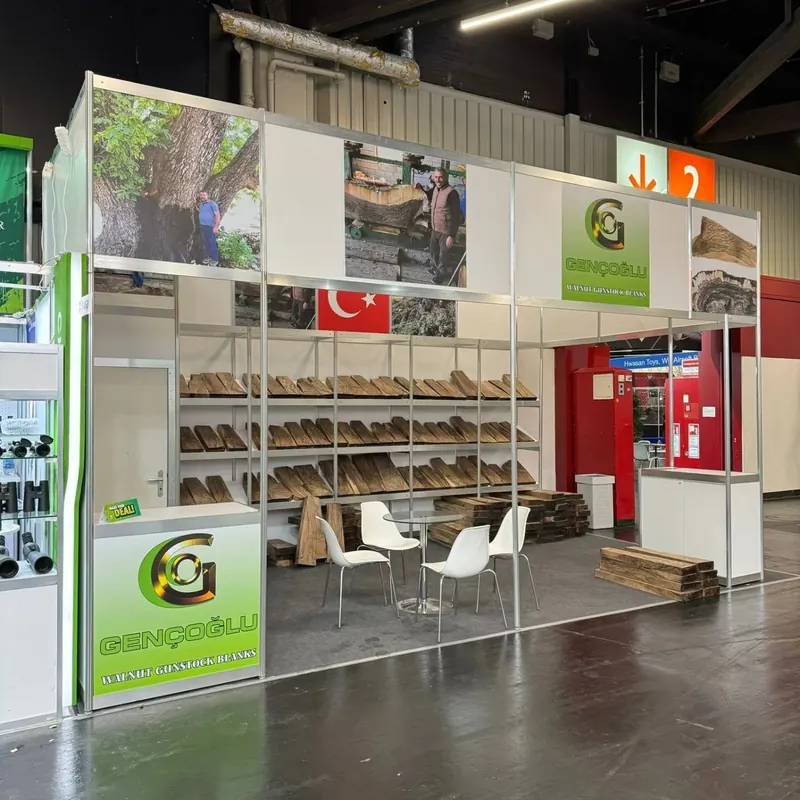 Weiß-grüner Messestand mit offenen Regalen, Holzprodukten und kleiner Sitzgruppe.