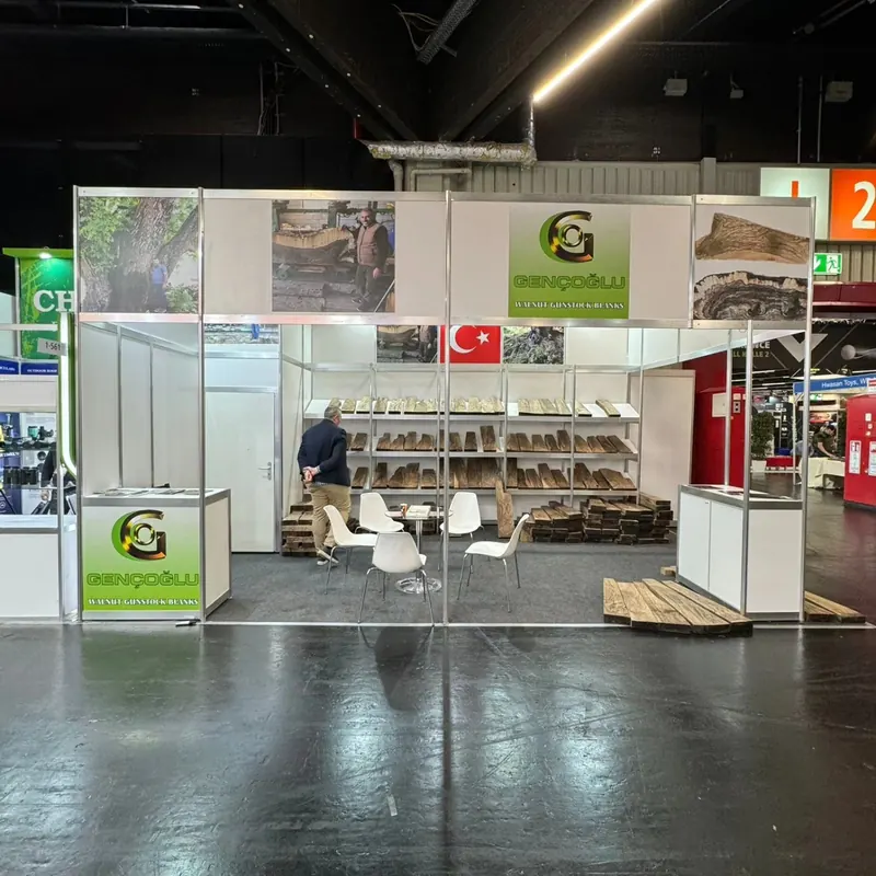 Weiß-grüner Messestand mit offenen Regalen, Holzprodukten und kleiner Sitzgruppe.