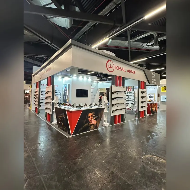 Weiß-grauer Messestand mit abgehängtem Rahmen, Langwaffen an Wanddisplays und Bildtheke.