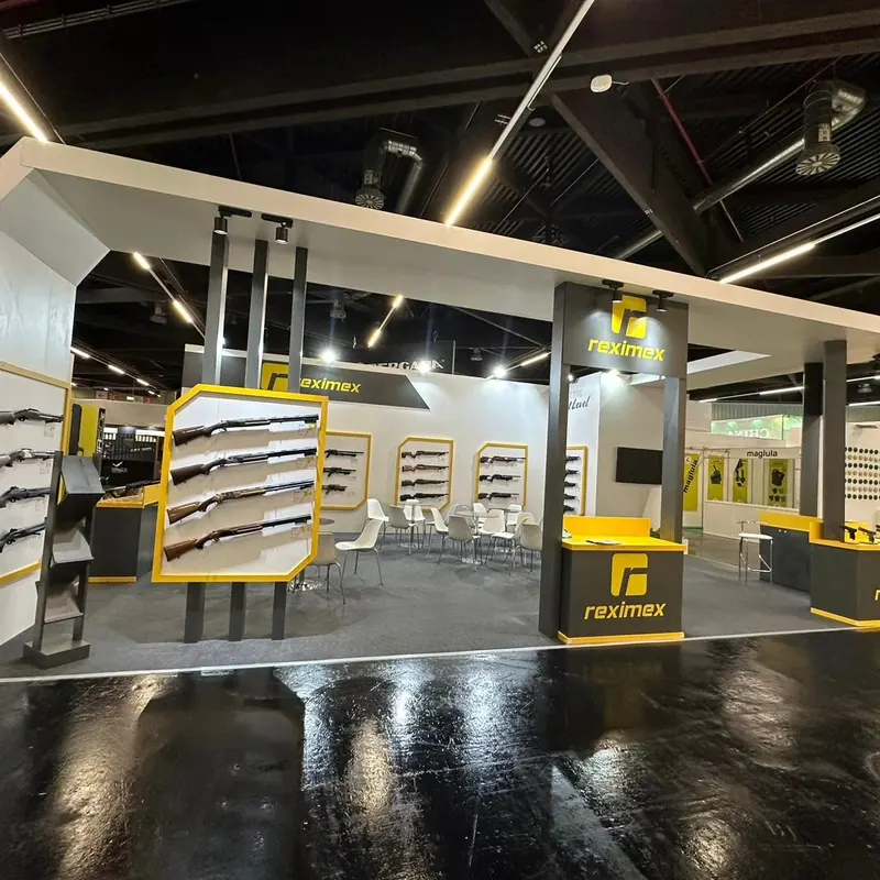 Weiß-gelber Messestand mit offenem Deckenrahmen und Wanddisplays für Langwaffen.