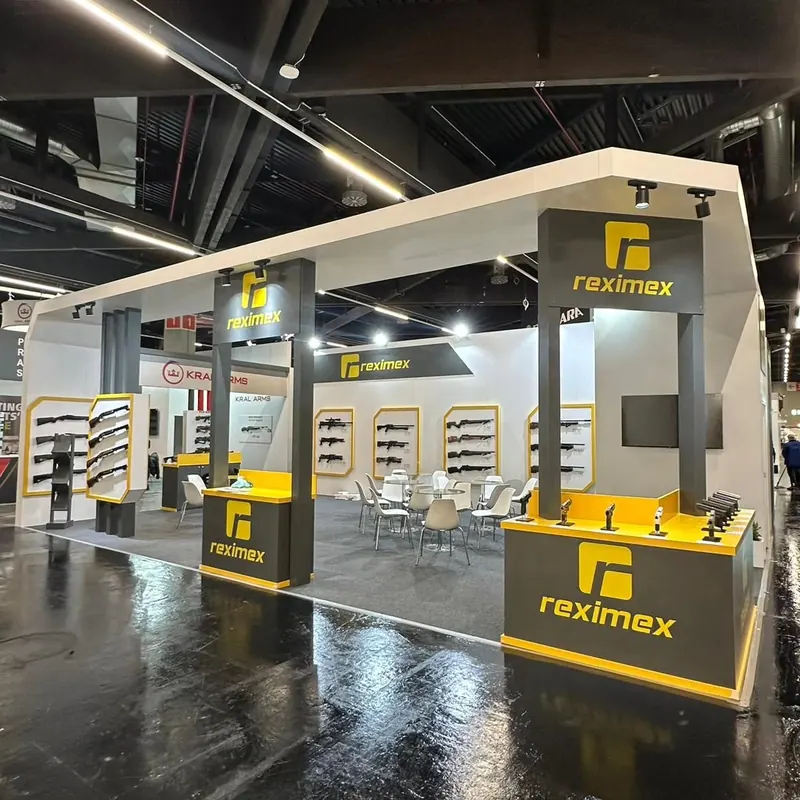 Weiß-gelber Messestand mit offenem Deckenrahmen und Wanddisplays für Langwaffen.