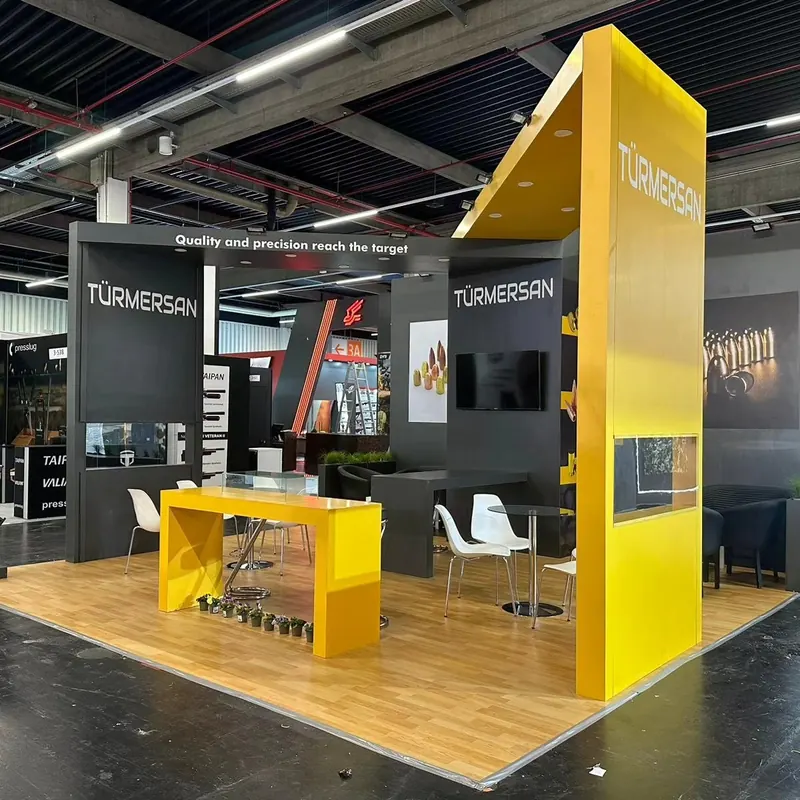 Dunkelgrau-gelber Messestand mit hohem Eckpylon, Bildschirm und Holzoptikboden.