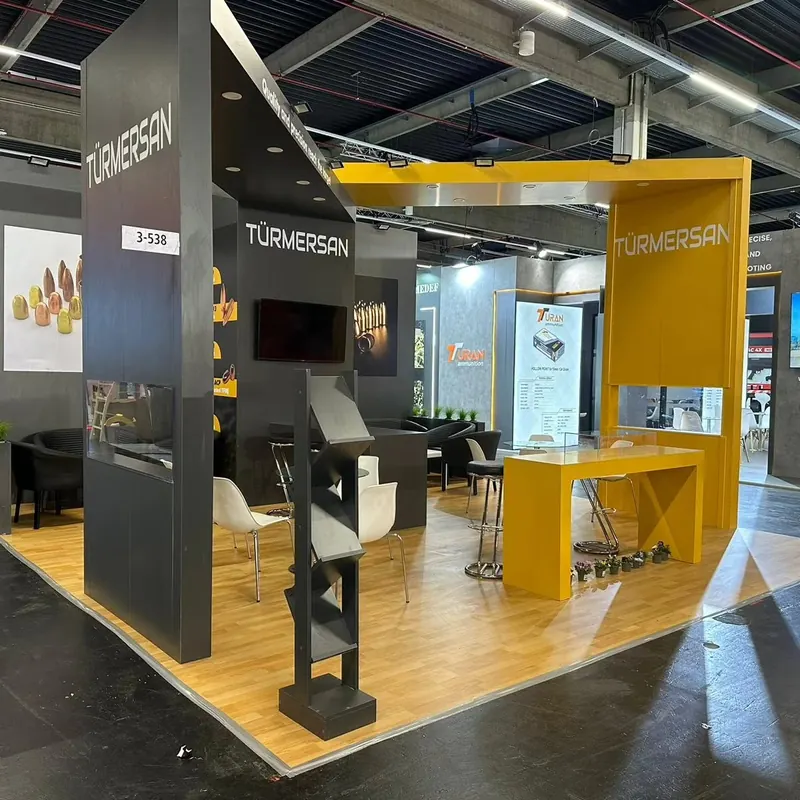 Dunkelgrau-gelber Messestand mit Glasvitrine, Stehtisch und Holzboden.