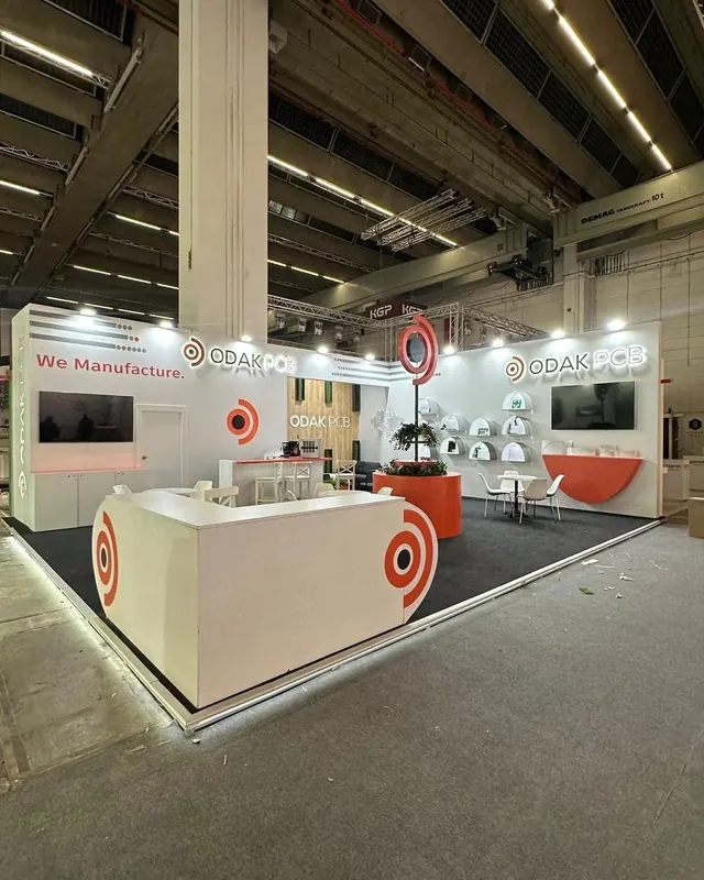 Weiß-oranger Messestand mit Glasvitrinen, Bildschirm und rund gestaltetem Empfang.