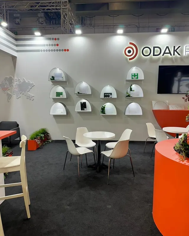 Weißer Messestand mit Produktschalen an der Wand, orangefarbenen Theken und weißen Sitzgruppen.