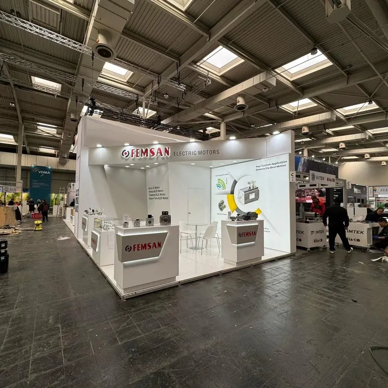 Weißer Messestand mit beleuchteter Beschriftung, technischen Mustern und breiter Theke.