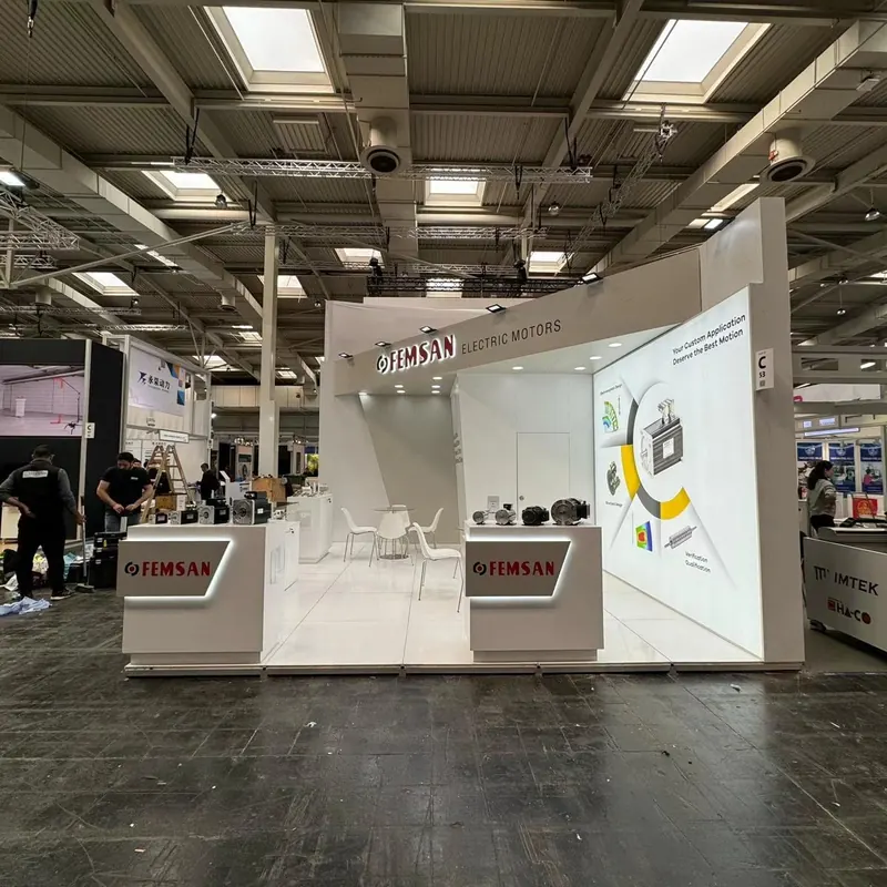 Offener weißer Messestand mit zwei Produktpodesten, Wandgrafiken und weißen Stühlen.