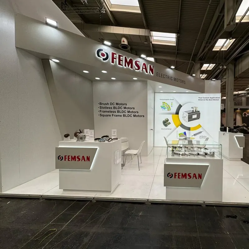 Offener weißer Messestand mit zwei Produktpodesten, Wandgrafiken und weißen Stühlen.