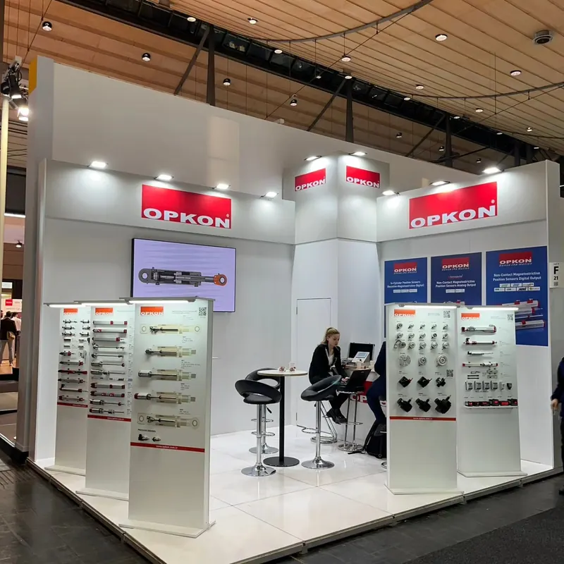 Weißer Eckstand mit roten Schildern, Produktmustern und kleinen Besprechungstischen.