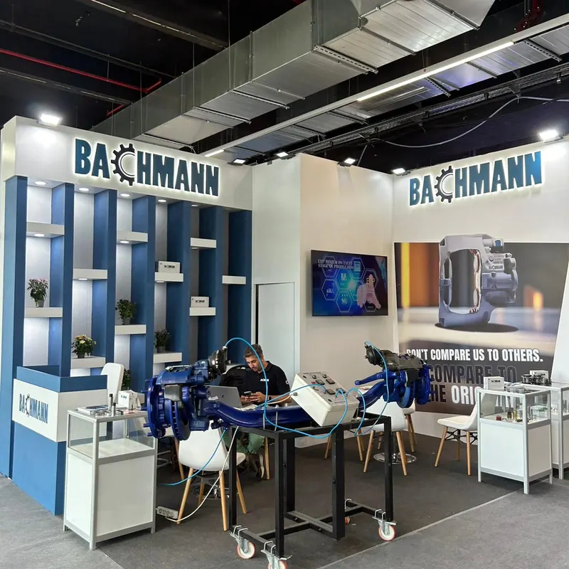 Blau-weißer Messestand mit Geräteexponaten, Glasvitrinen und weißen Stühlen.