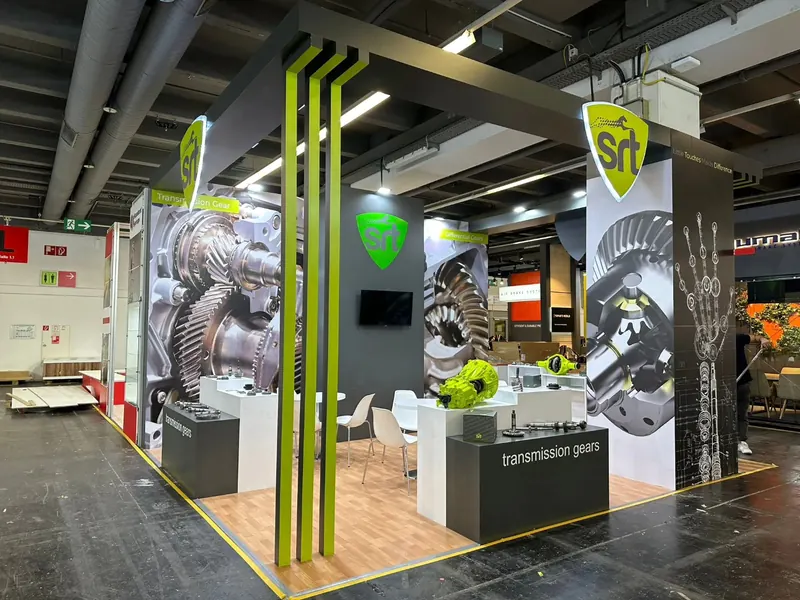 Grauer Messestand mit leuchtgrünen Rahmenelementen, Zahnradgrafiken und weißen Sitzgruppen.
