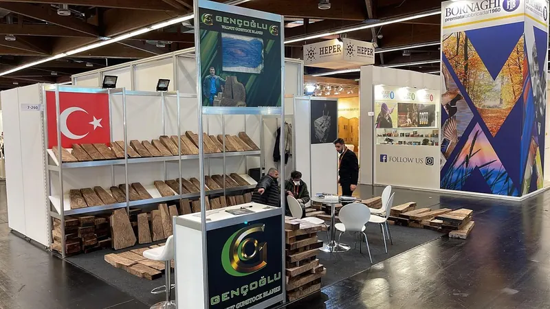 Weißer Messestand mit gestapelten braunen Produktmustern, hohen Schildern und kleiner Sitzgruppe.