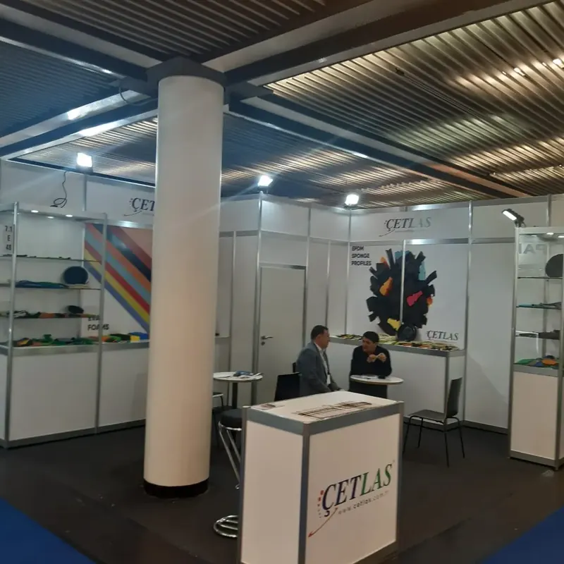 Weißer Messestand mit runder Stütze, farbiger Wandgrafik und kleiner Sitzgruppe.