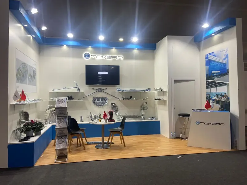 Weiß-blauer Messestand mit langen Wandregalen, Metallteilen und zwei schwarzen Stühlen.