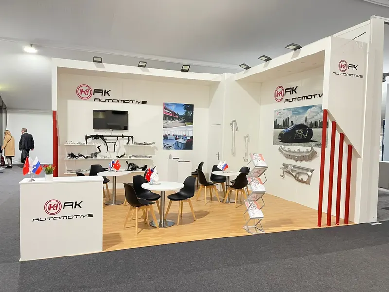 Weiß-roter Messestand mit Bauteilmustern, Holzoptikboden und schwarzen Stühlen.